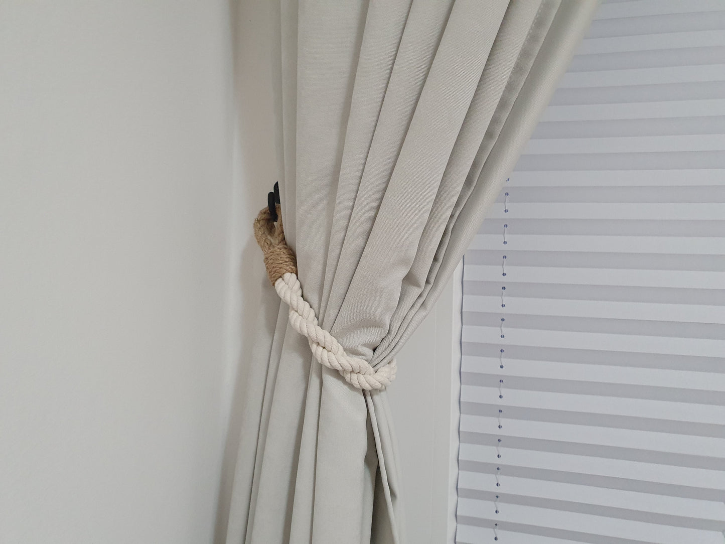 Beige curtain with a rope tieback next to a window with blinds.