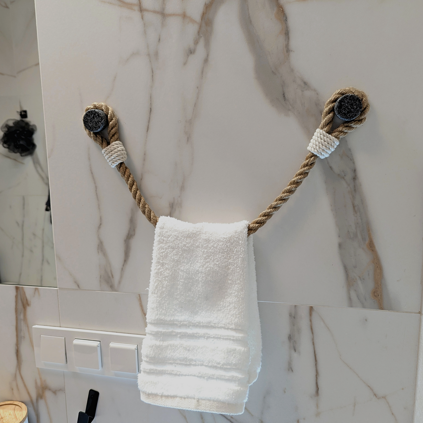 A white hand towel hangs from a rope-style wall hook set against a white marble-patterned wall.