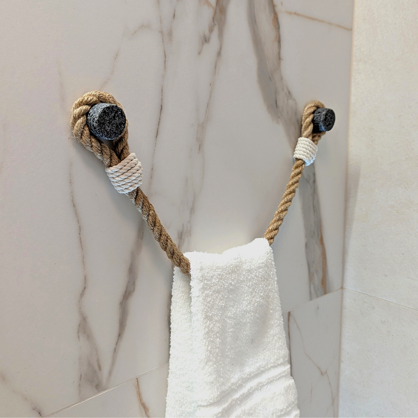 A white towel hanging from a rope towel rack mounted on a beige marble-patterned wall.