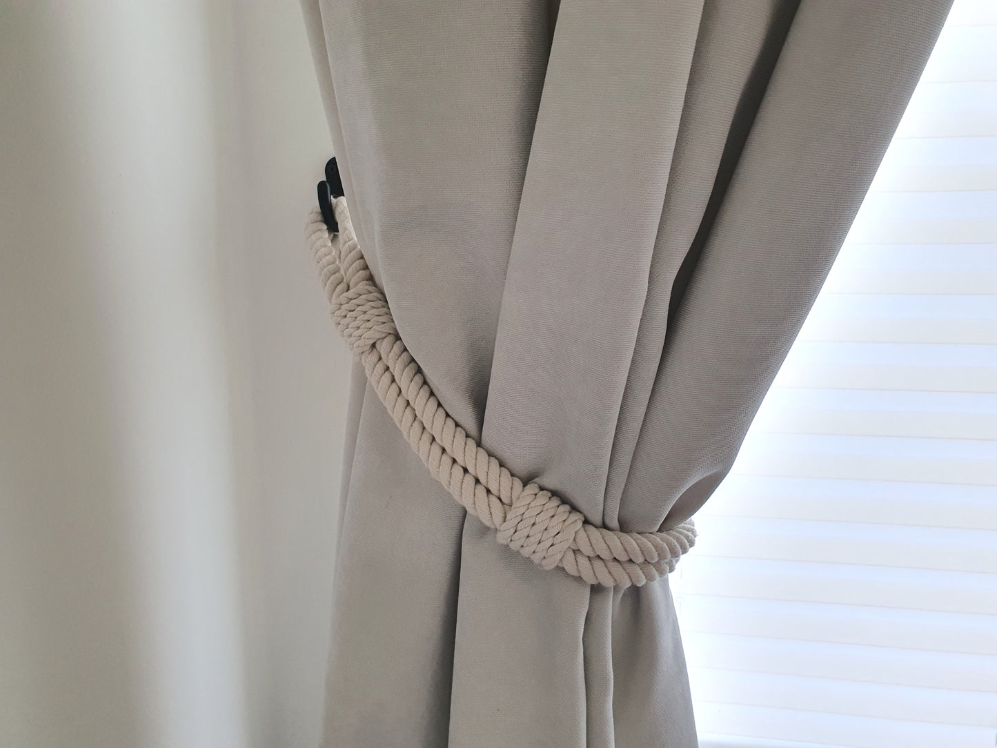 White curtain with a decorative rope holdback against a window