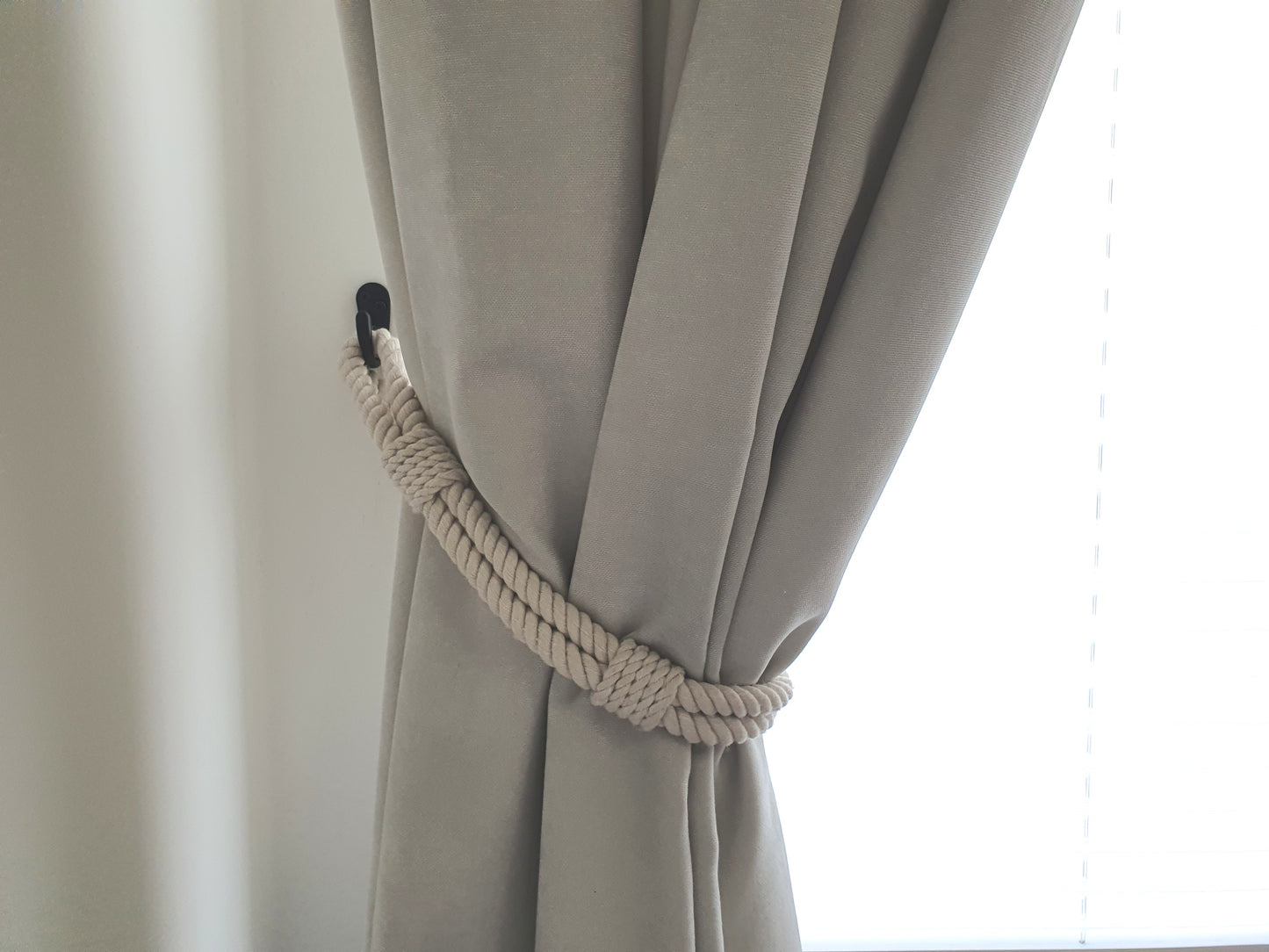 White curtain with a rope tieback against a white background boho style