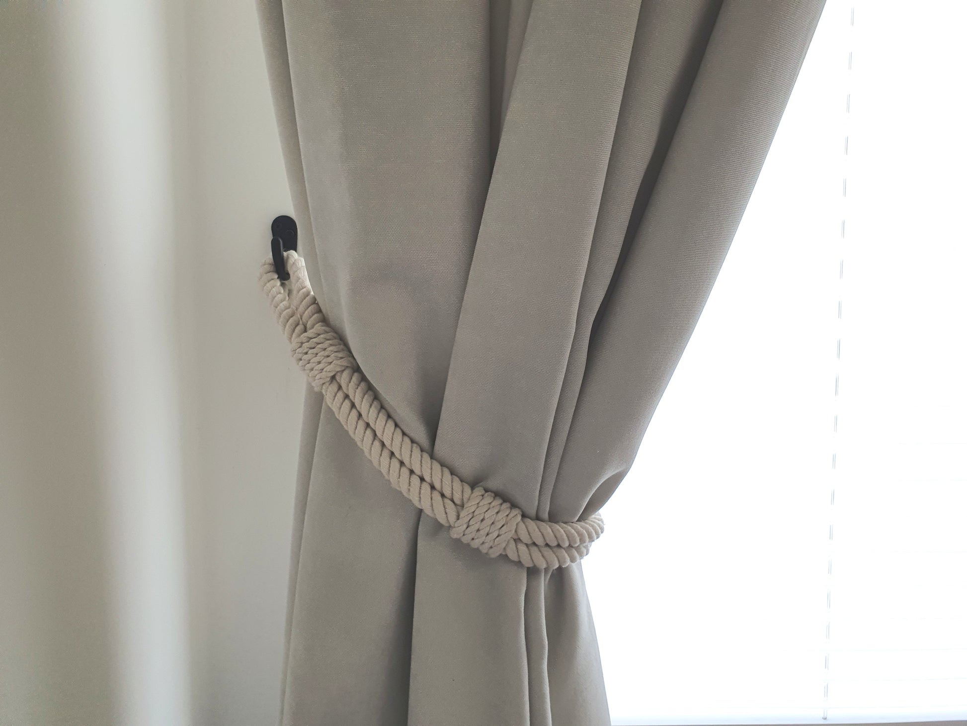 White curtain with a rope tieback against a white background boho style