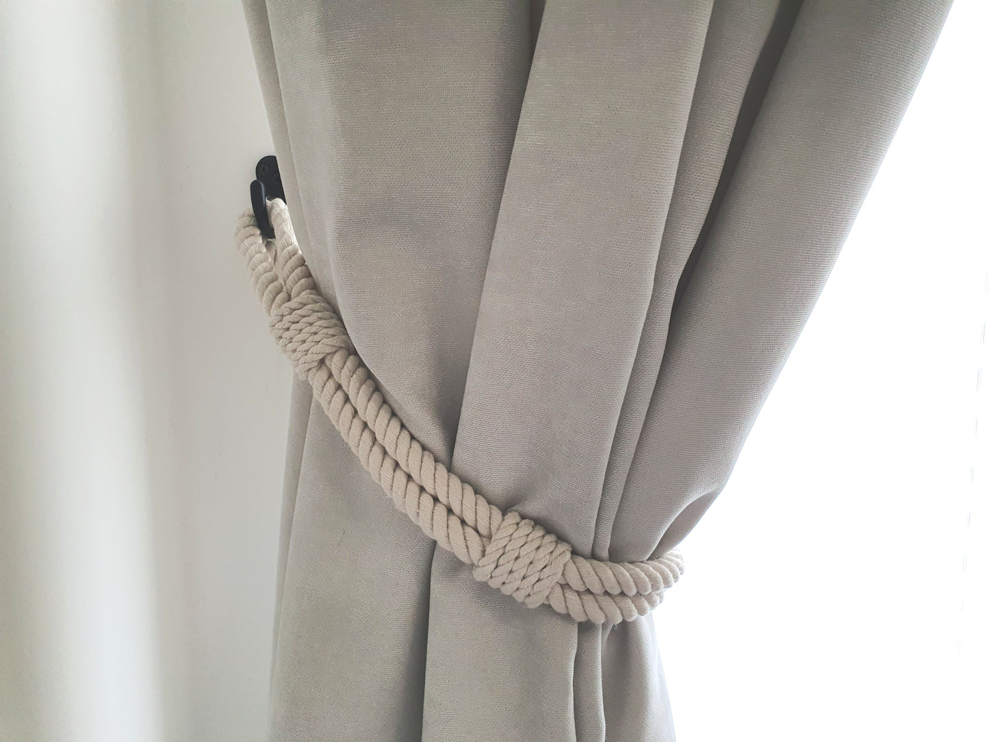 White curtain with a rope tieback against a white background boho style