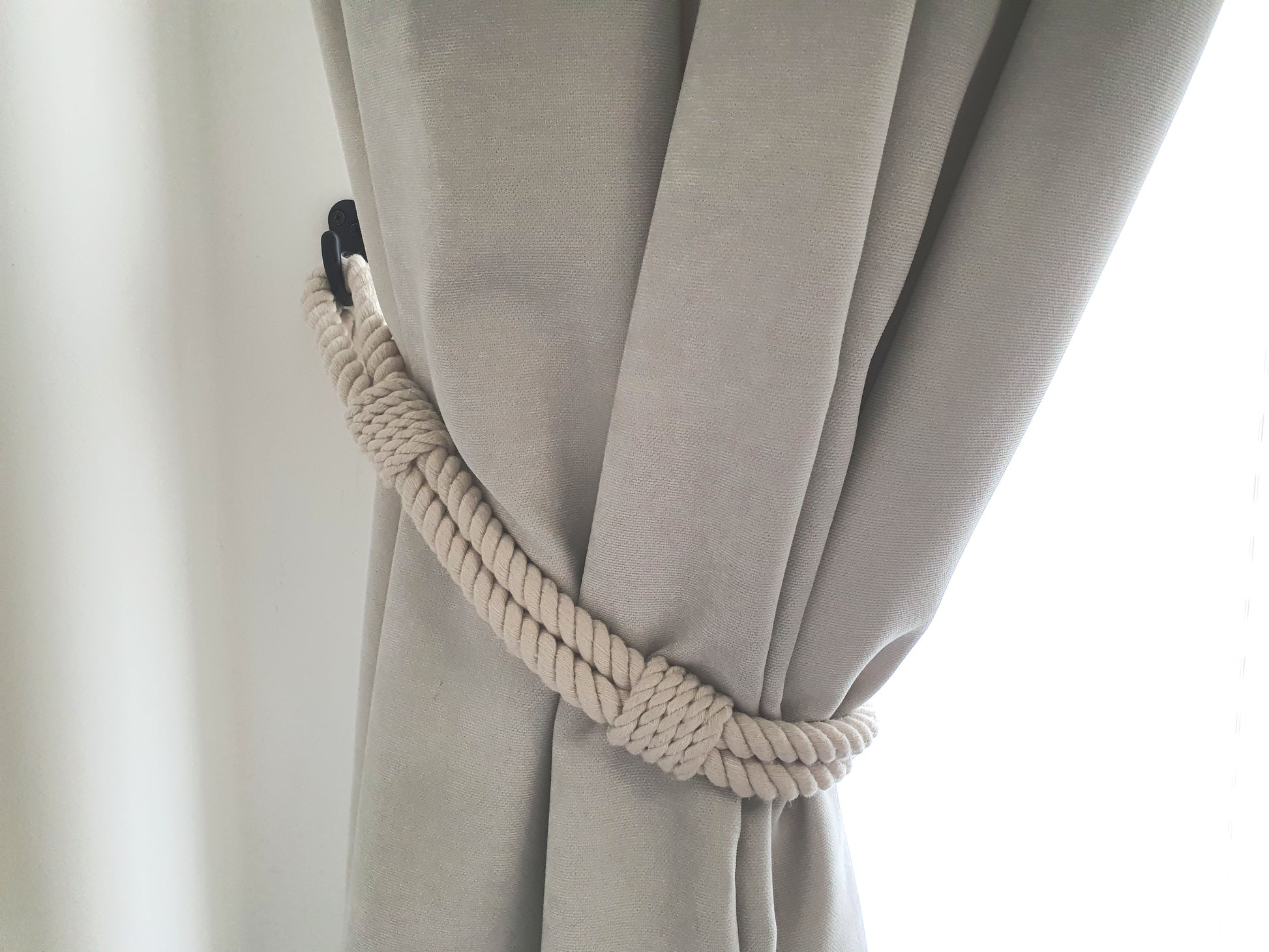 White curtain with a rope tieback against a white background boho style