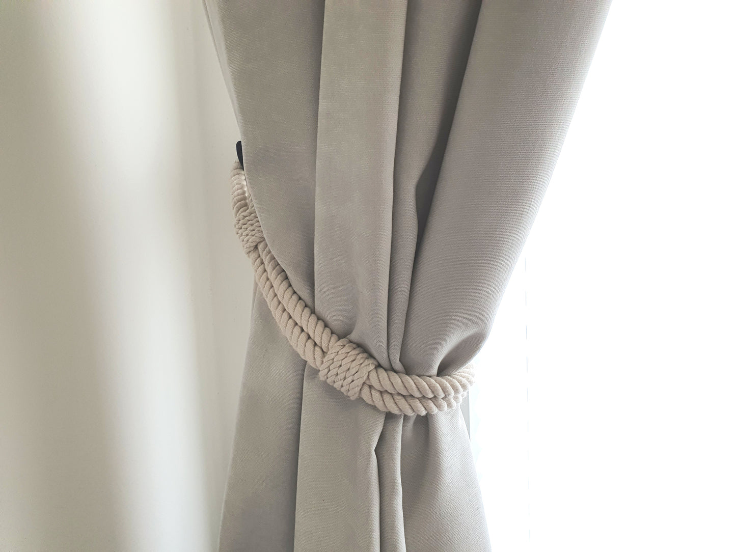 White curtain with a rope tieback against a white background boho style