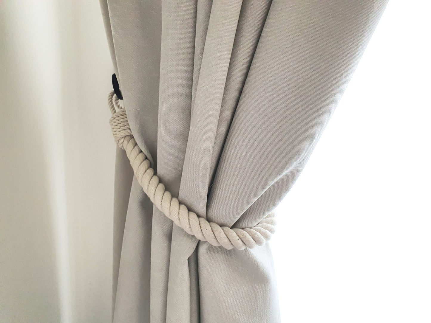 White curtain with a rope holdback against a window