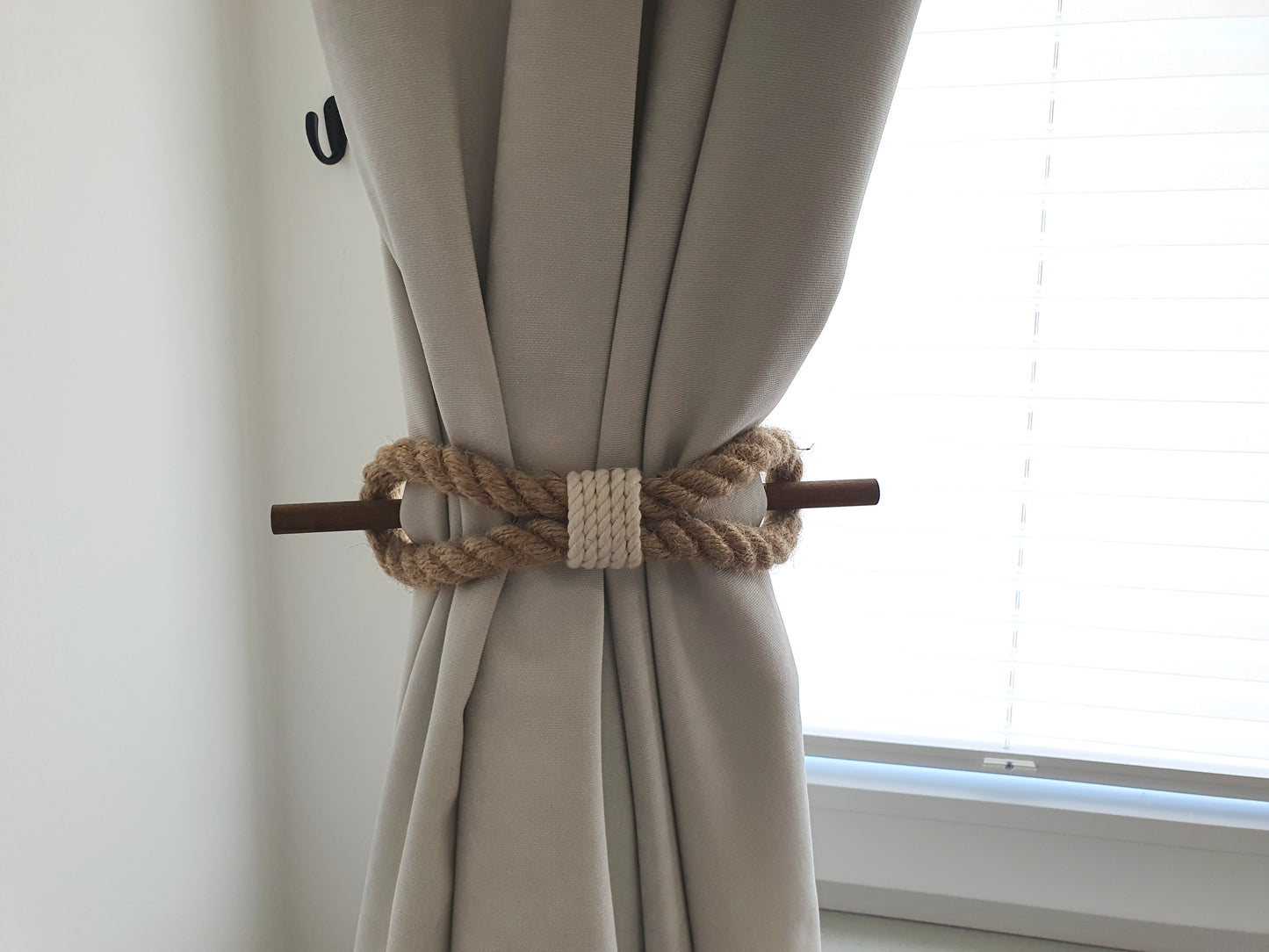 Beige curtain with a decorative rope tieback in front of a window.