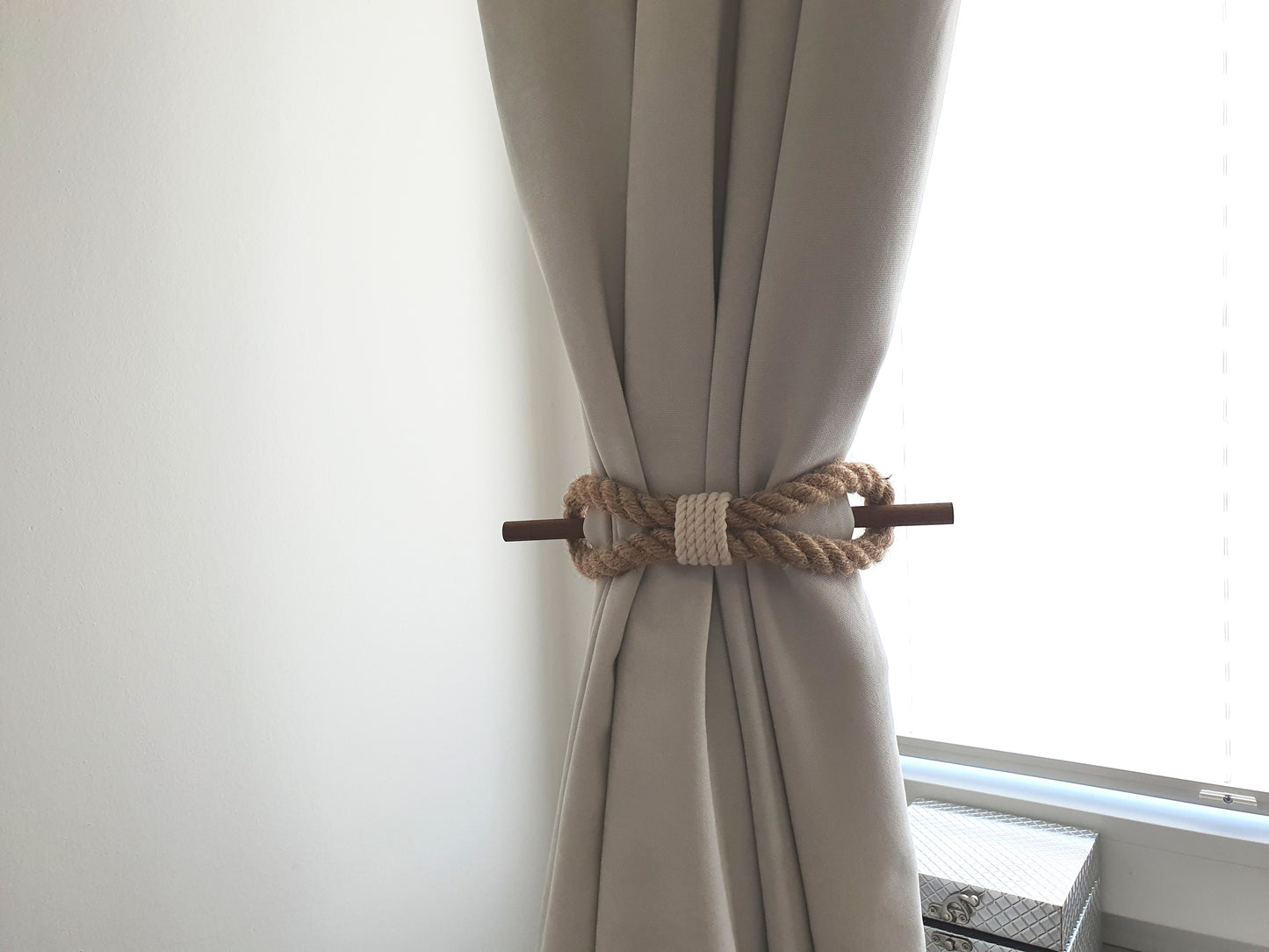 Beige curtain with a decorative rope holdback against a white wall.