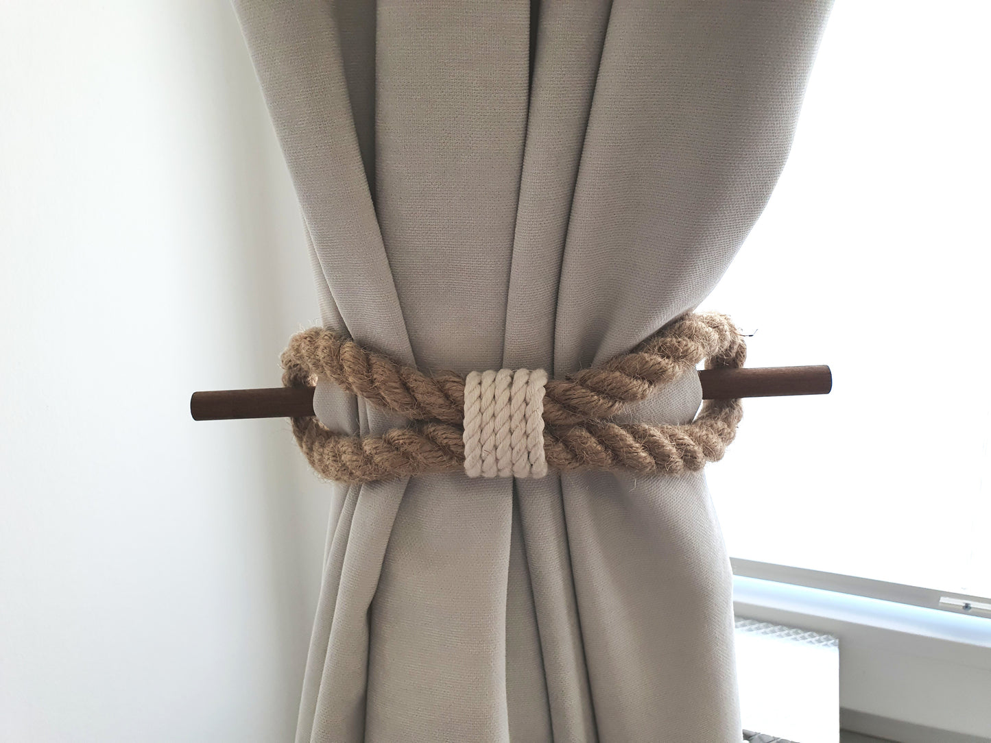 Beige curtain with a boho style rope tieback in front of a window.