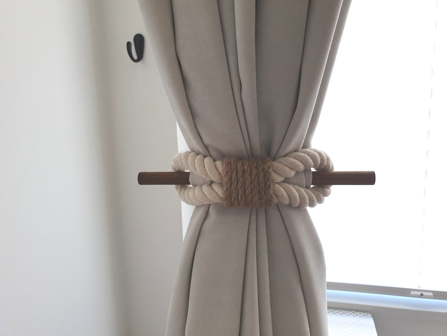 White curtain with a decorative beige rope tieback in front of a window.
