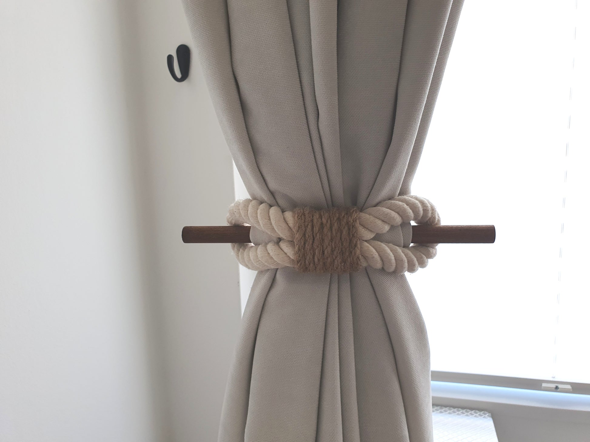 White curtain with a decorative beige rope tieback in front of a window.
