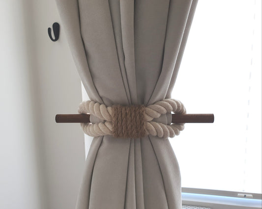 White curtain with a decorative beige rope tieback in front of a window.
