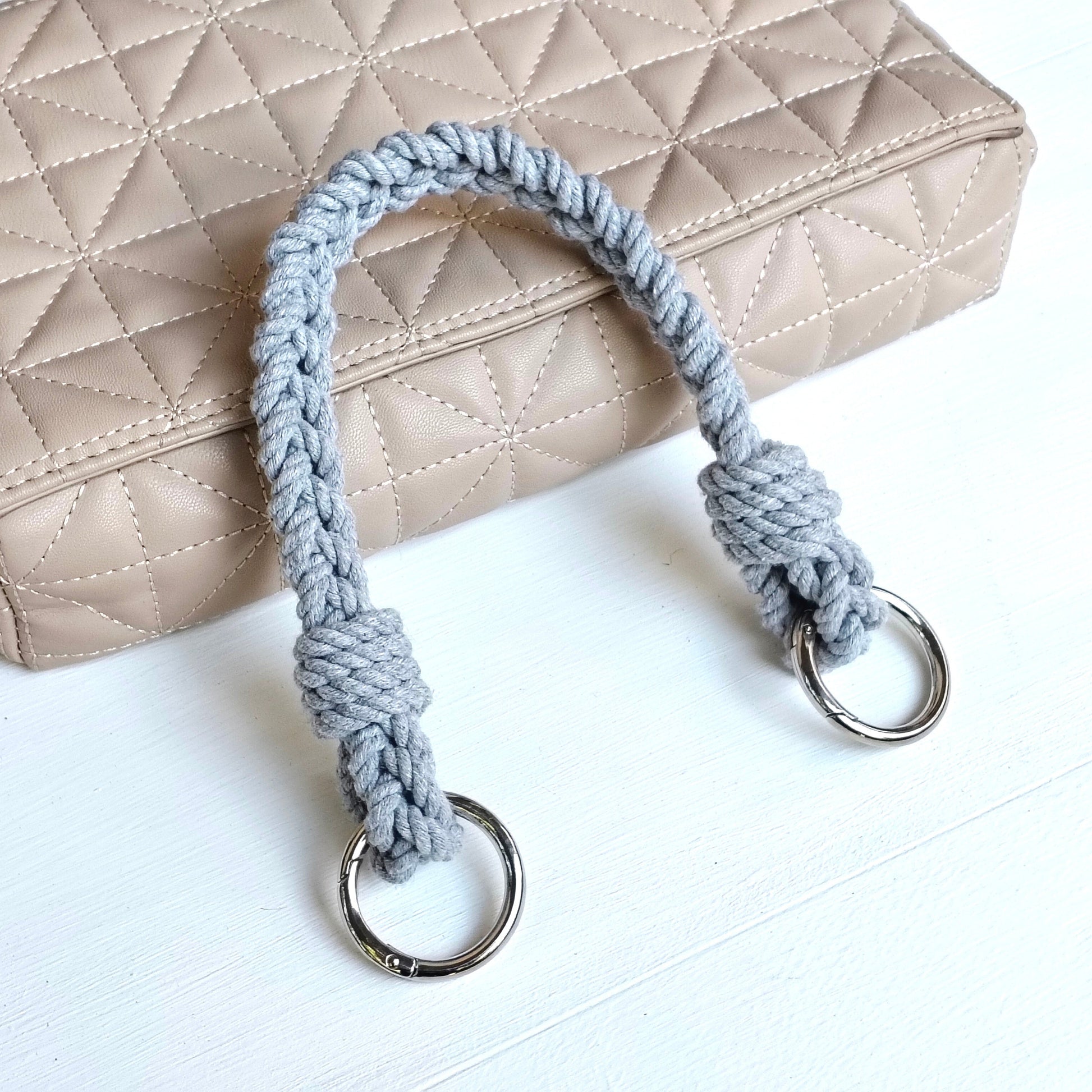 A light gray braided rope handle bag with silver metal O-rings,