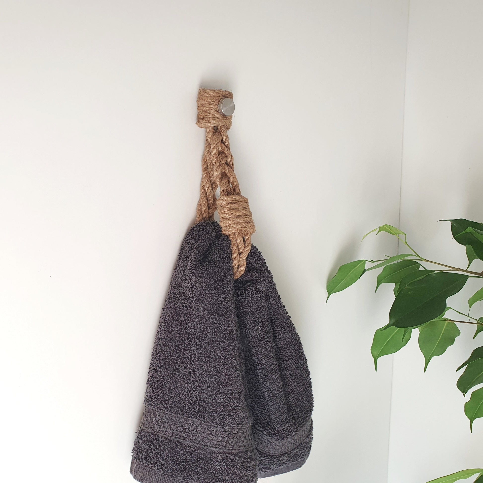 A dark gray textured towel hanging from, towel holder a thick natural jute rope hook on a white wall, eko modern farmhause