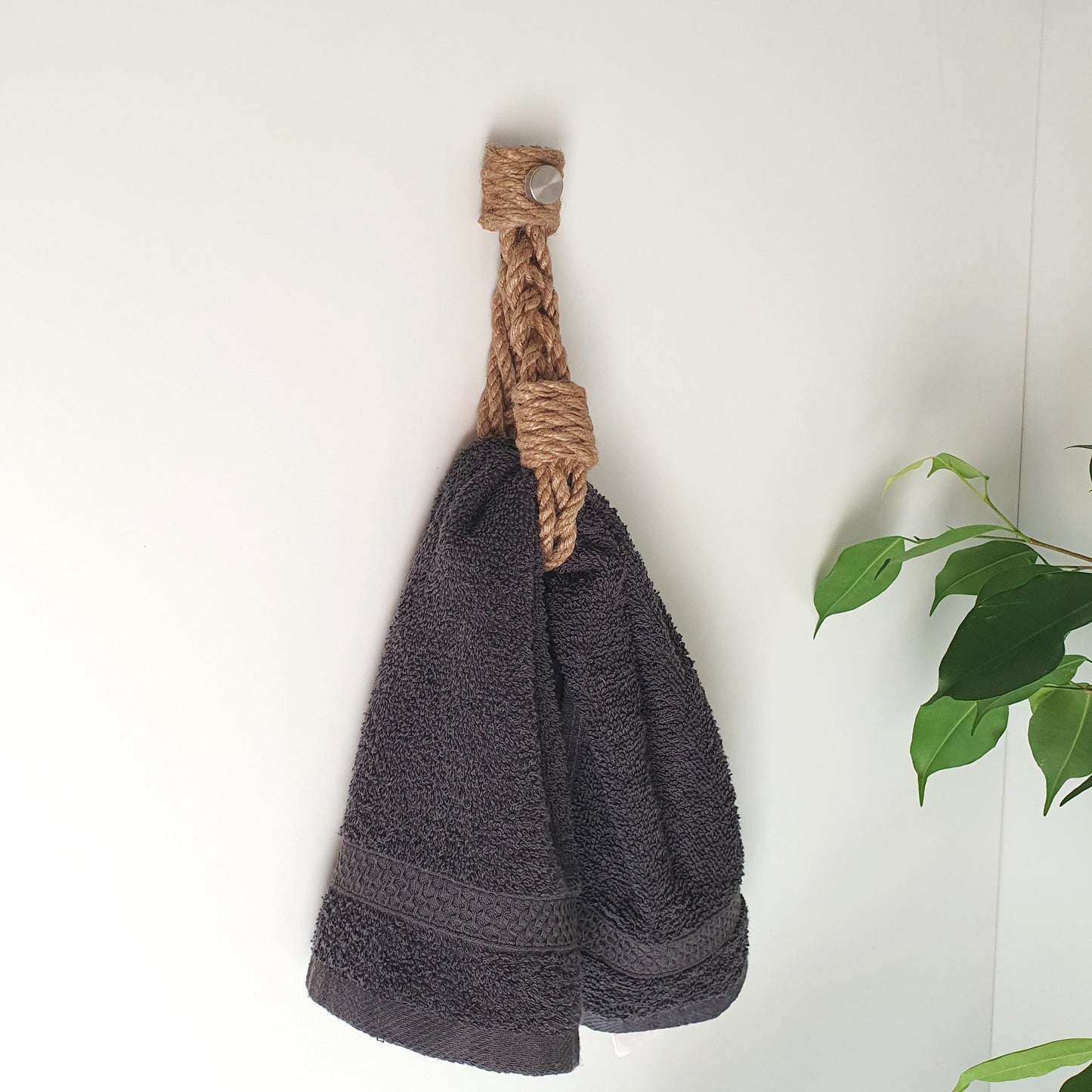 A dark gray terry cloth towel hanging towel holder from a natural jute rope wall hook on a white wall, eko natural design bathroom