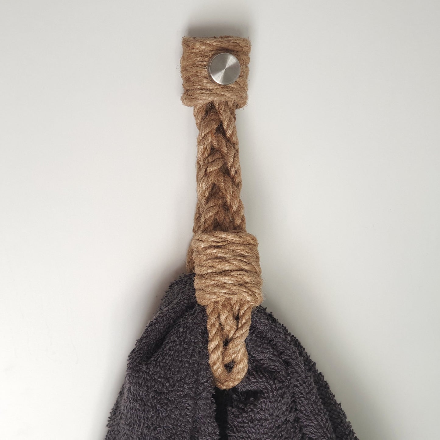 A close-up of a dark gray towel hanging holder from a natural jute rope handle with a silver metal snap button, set against a plain light gray background.