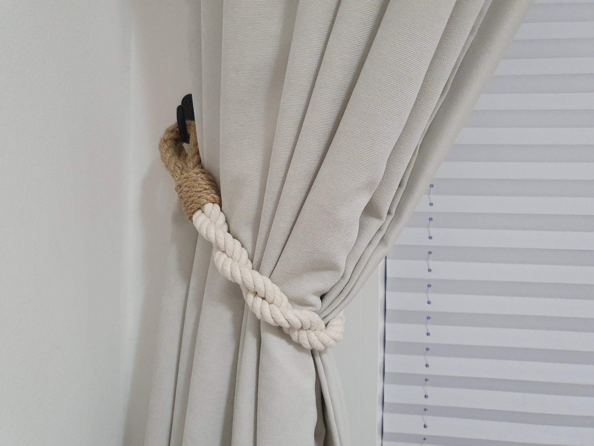 Curtain tied back with a rope tie-back against a white wall with blinds.