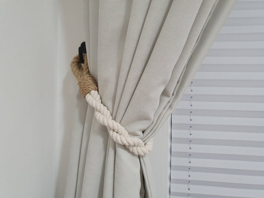 Curtain tied back with a rope tie-back against a white wall with blinds.