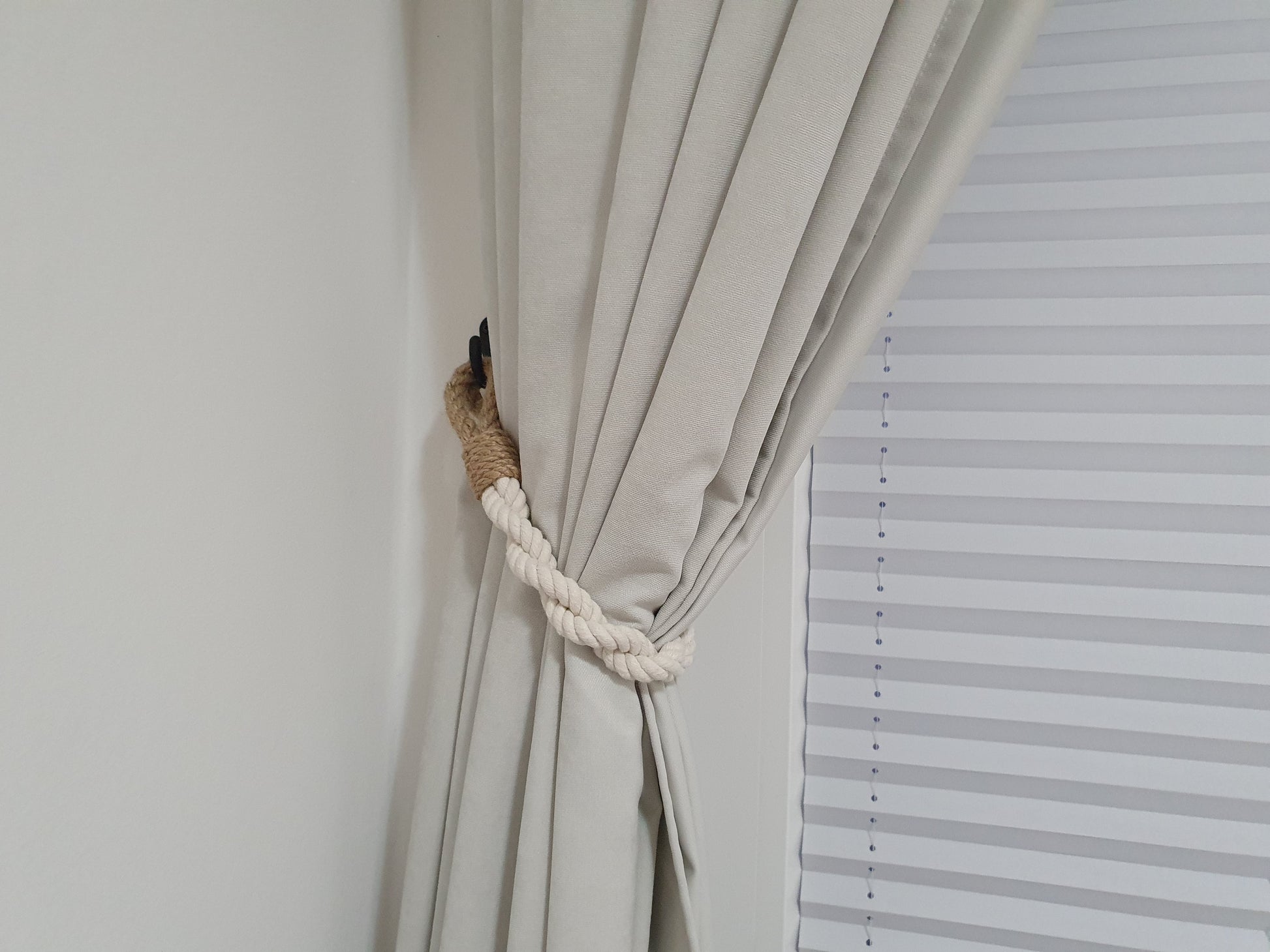 Beige curtain with a rope tieback next to a window with blinds.
