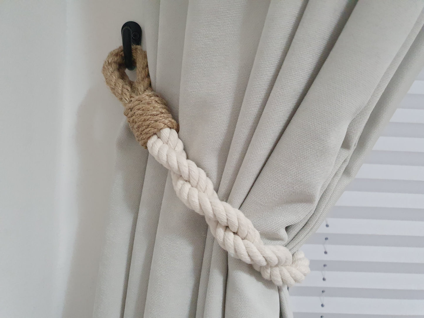 Curtain tieback with braided rope and wooden accent on a neutral curtain.