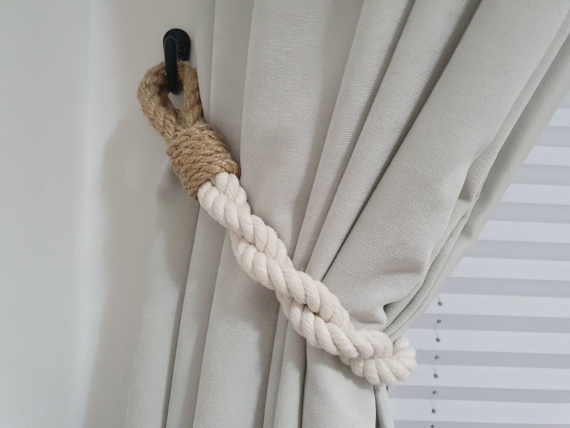 Curtain tieback with braided rope and wooden accent on a neutral curtain.