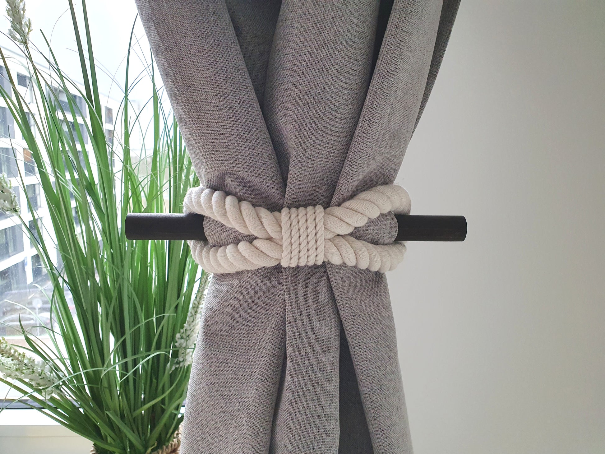 Gray curtain with a decorative white cotton rope tieback with black stick