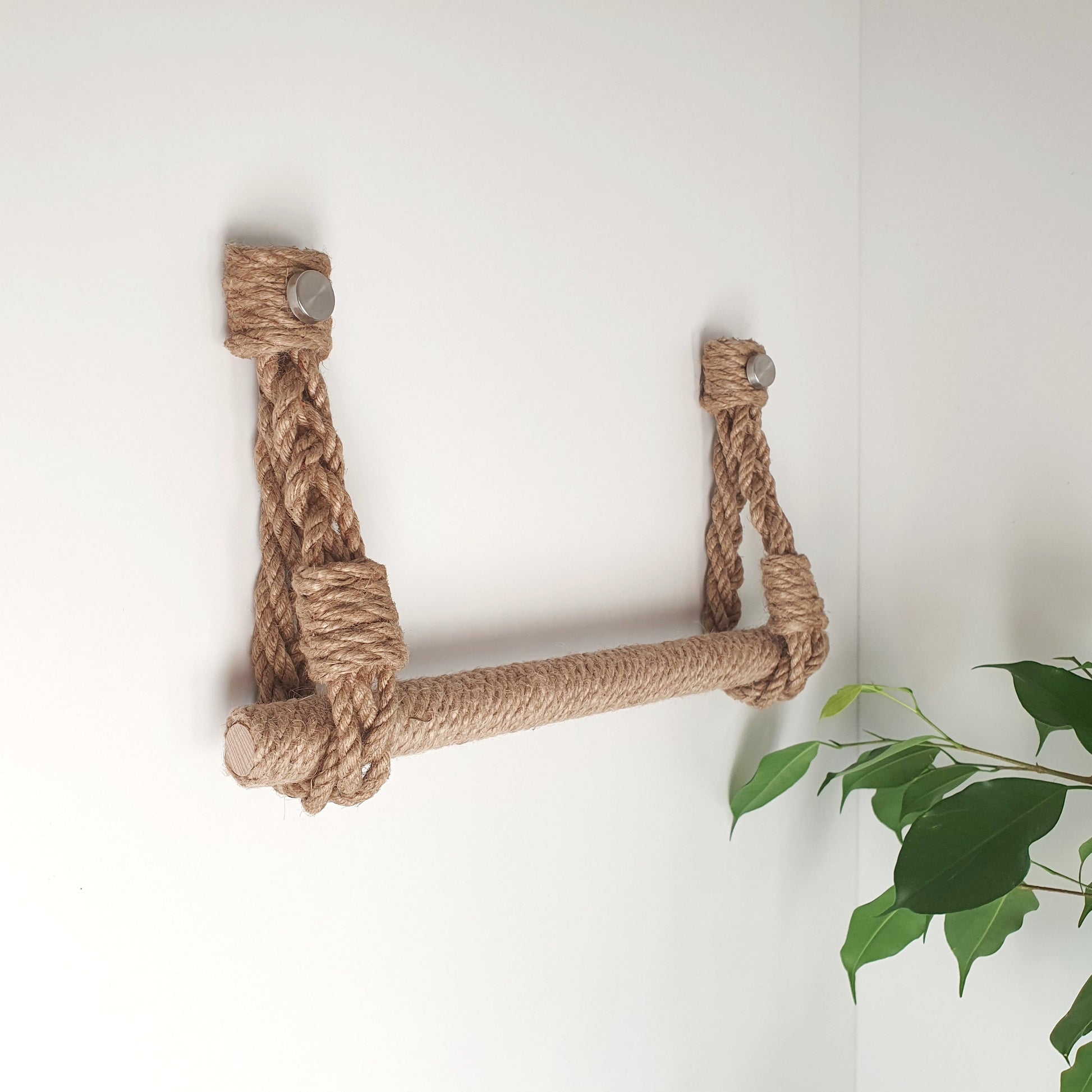 A rope wall-mounted shelf or ladder made of natural jute rope, attached to a white wall with two small metal anchors, towel older modern farmstyle