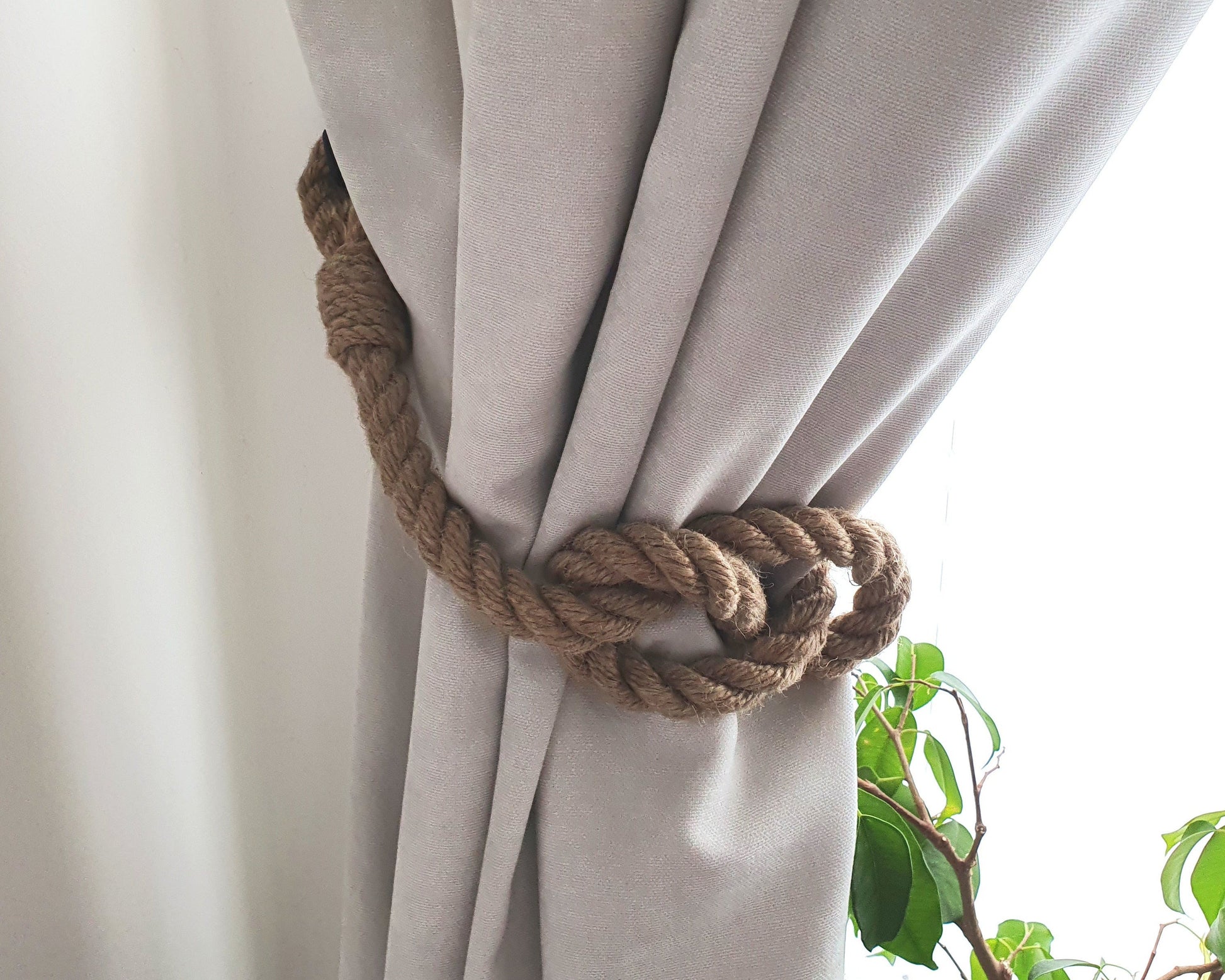 Light white curtain with a rope tieback, partially open to reveal greenery outside.