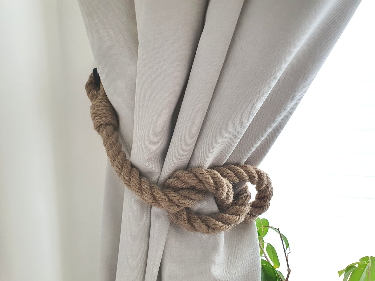 Nautical rope curtain tieback on a white curtain with a blurred plant in the background